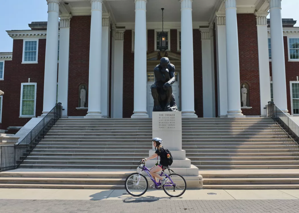 Student biking past the Thinker in front of Grawemeyer Hall