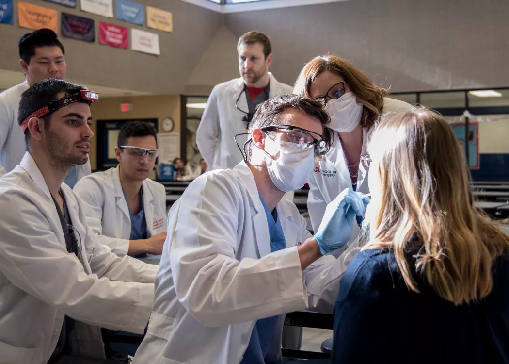 Five dental students and a faculty member examine another student