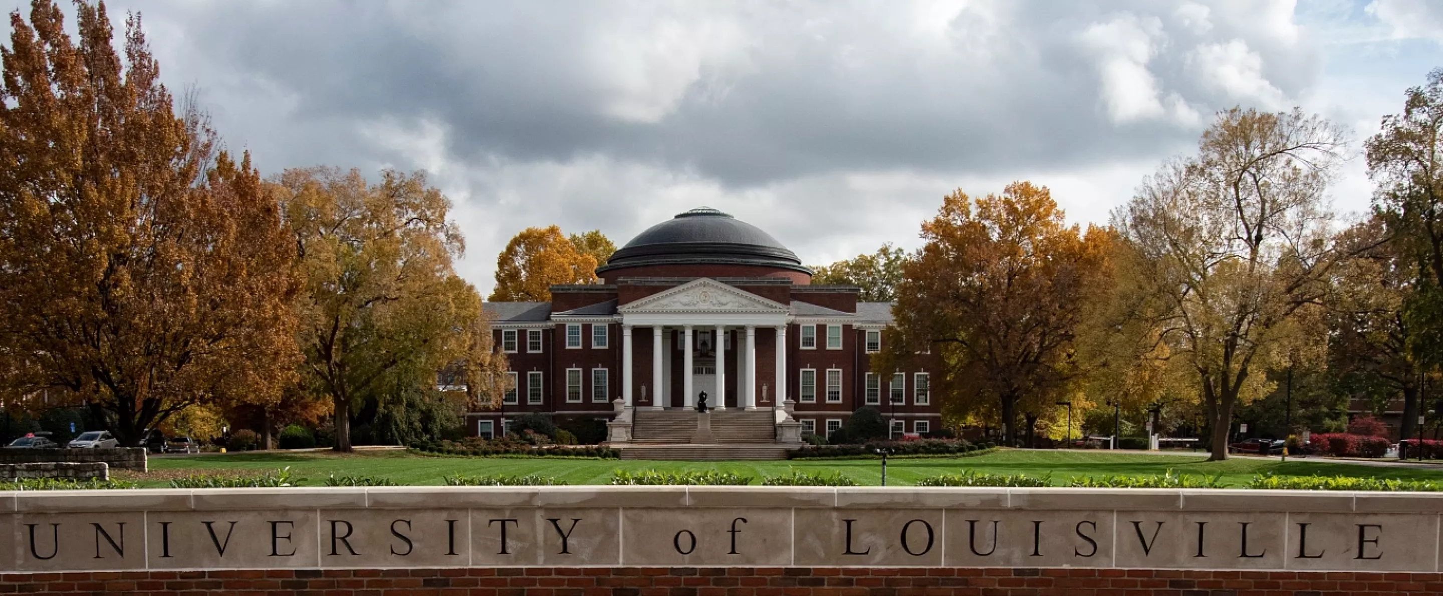 Wide-angle portrait of the exterior of Grawemeyer Hall and the Oval with the 3rd Street entrance sign and Minerva in the foreground