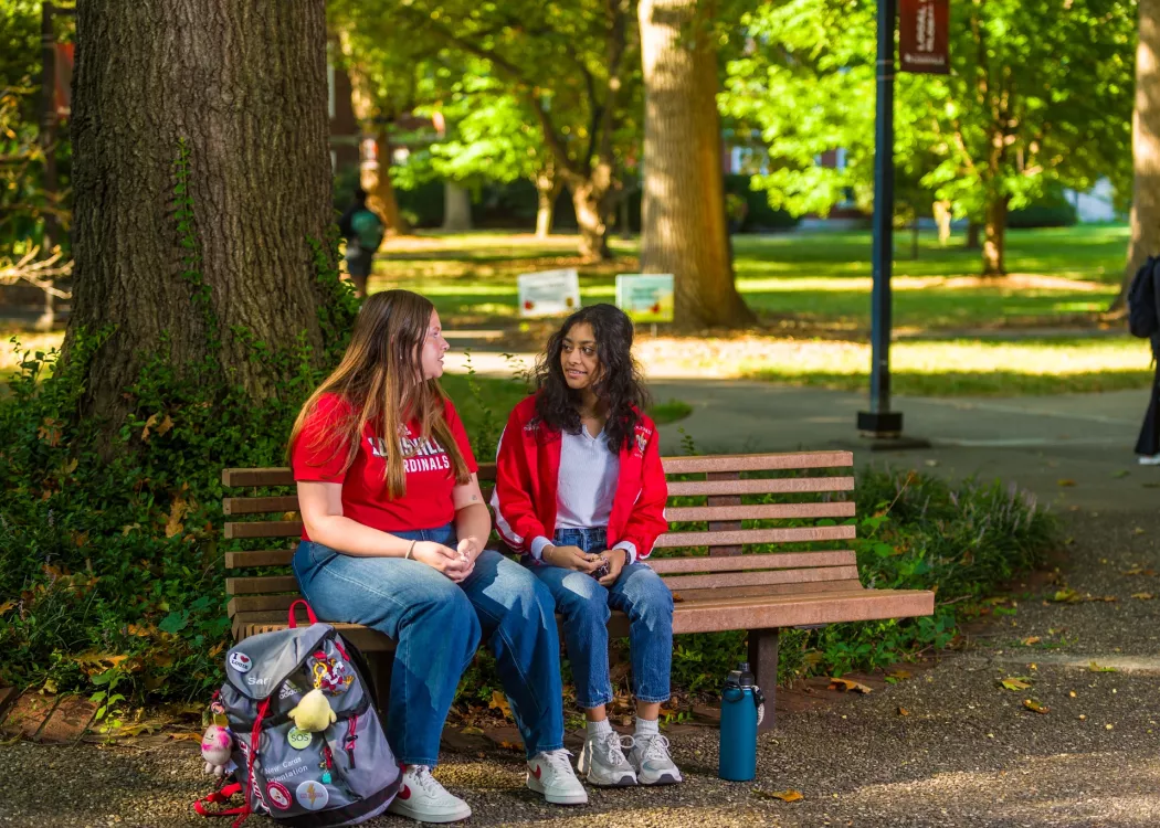 Two students talking on a bench on Belknap Campus