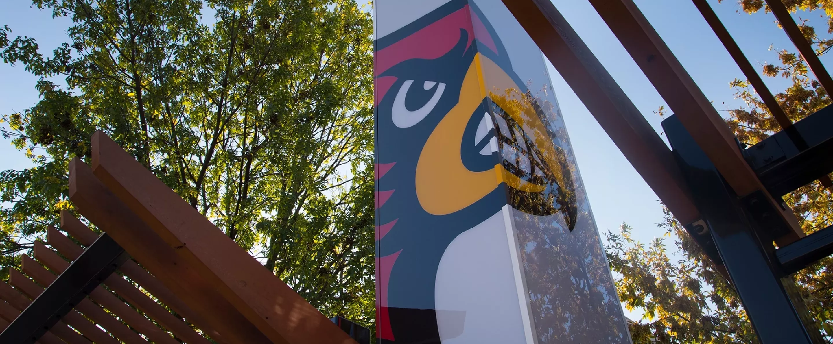 Pillar with Cardinal Bird head against wooden structure and trees.