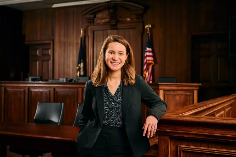 A young woman in a business suit stands in a mock courtroom