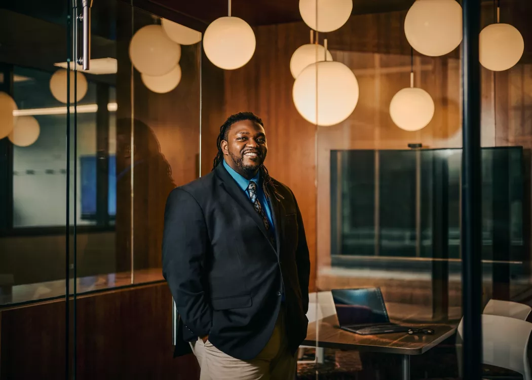 A smiling man in a suit standing in a modern office space.